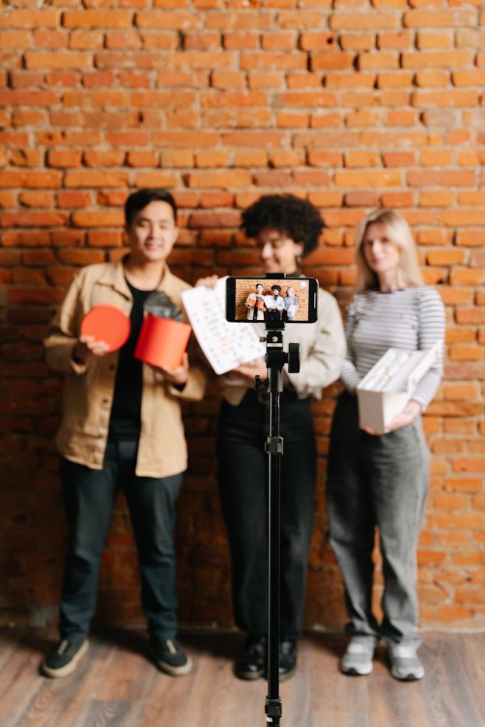 Three young adults recording a vlog with smartphone and tripod indoors.