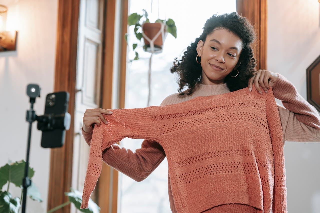 Young woman showing a knit sweater during an indoor fashion vlog session.