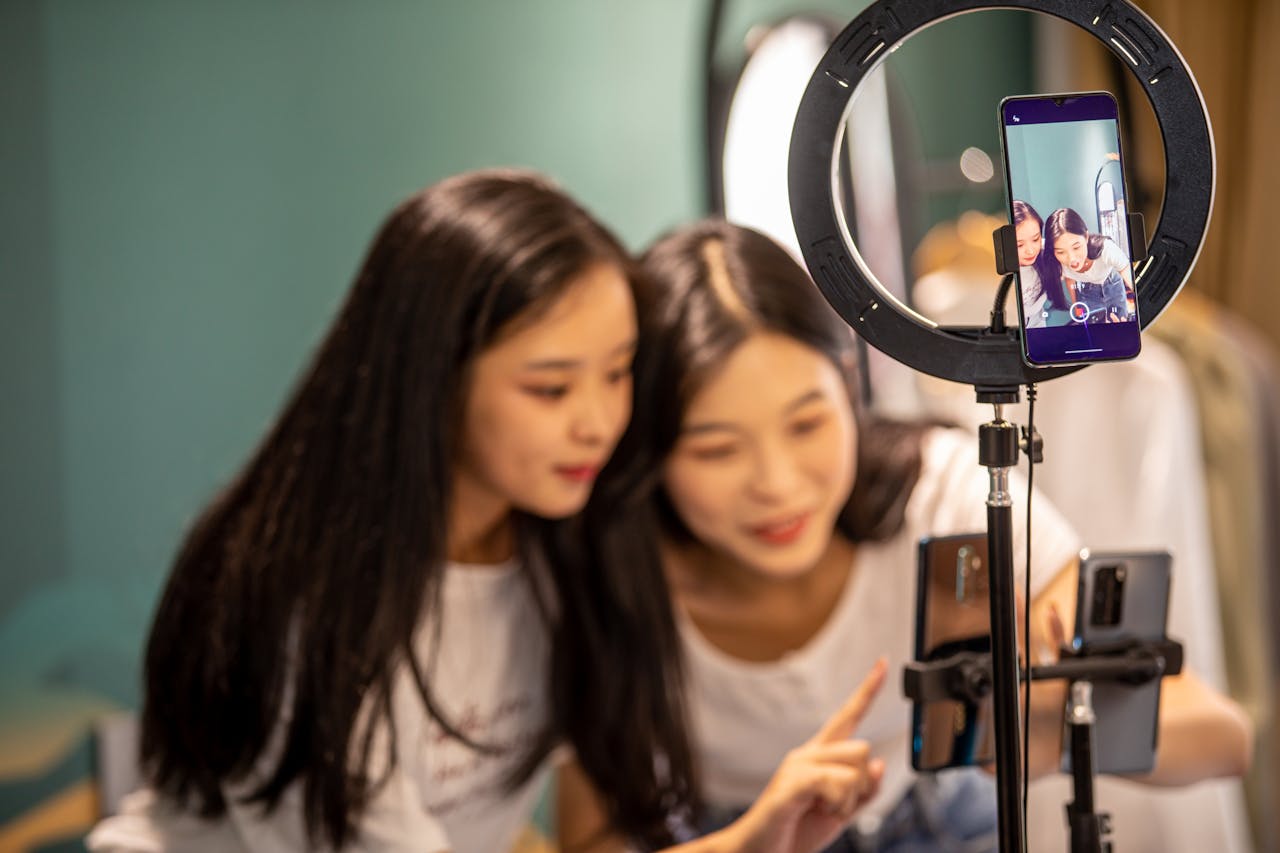 Two women actively using a smartphone and ring light setup indoors.